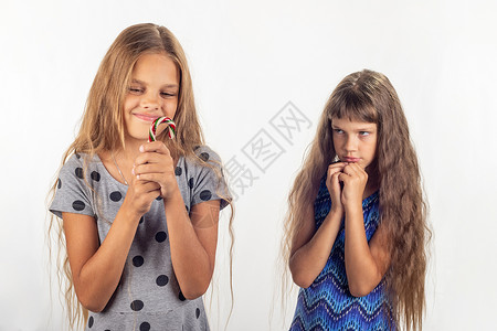 不给糖一个女孩手里拿着棒糖另一个女孩的背后看着那个女孩责备地她背景