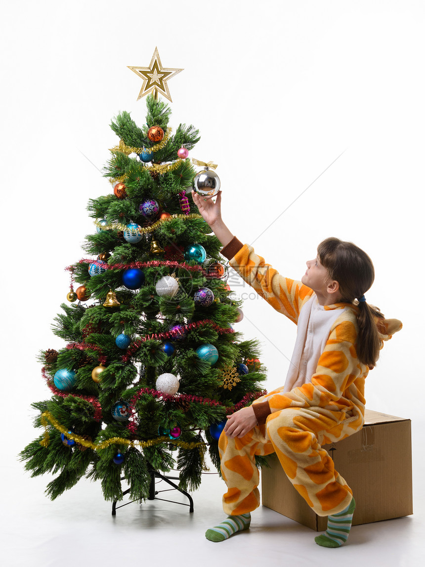 女孩坐在圣诞树前面的盒子上挂着圣诞树球图片