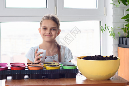 女孩拿着一袋种子和大地的罐坐在桌边图片