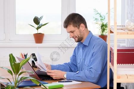 成功青年男子坐在办公室的桌子上看文件图片