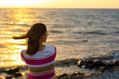 一个女孩坐在晚上的夜日落在海边的从后面看图片