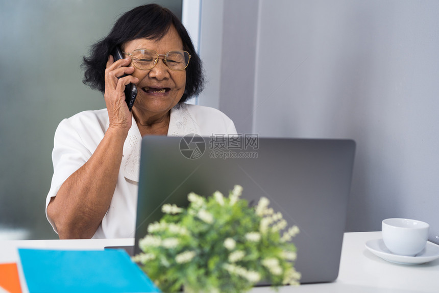 快乐的老年妇女在移动电话上交谈和在笔记本电脑上工作图片