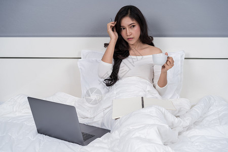 妇女在床上思考和操作笔记本电脑卧室高清图片素材