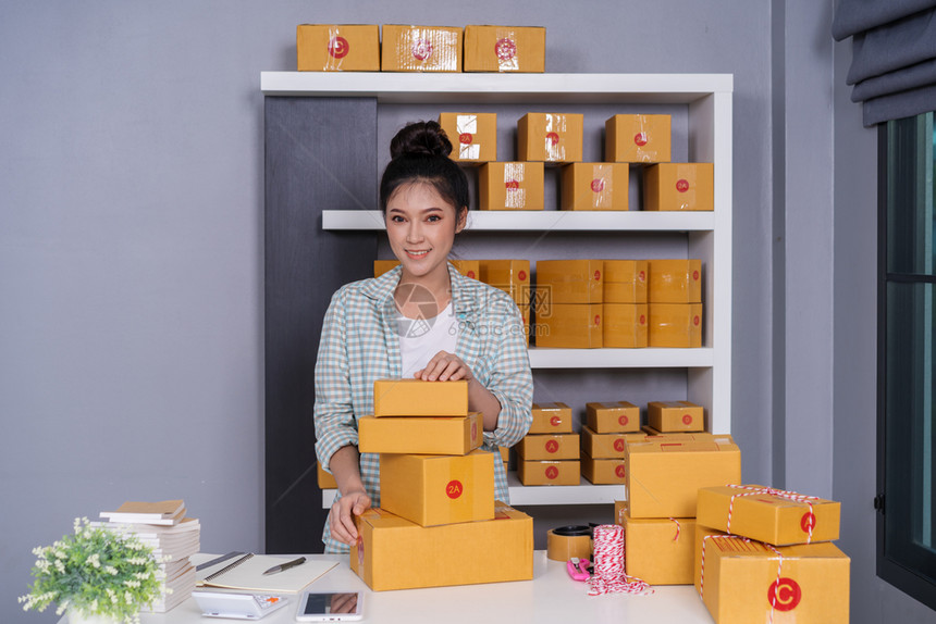 青年女创业者在她自己的工作岗位上拥有包裹箱的女青年创业者在家网上购物图片