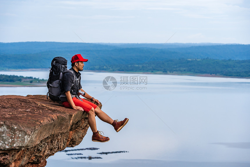 男人旅行者背着包坐在悬崖边缘岩石山顶图片
