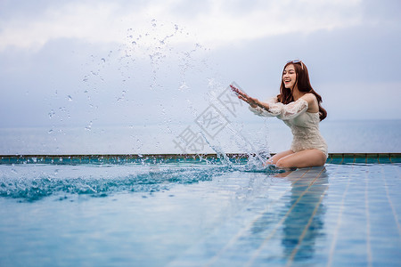 在有海背景的游泳池里玩水年轻女子图片