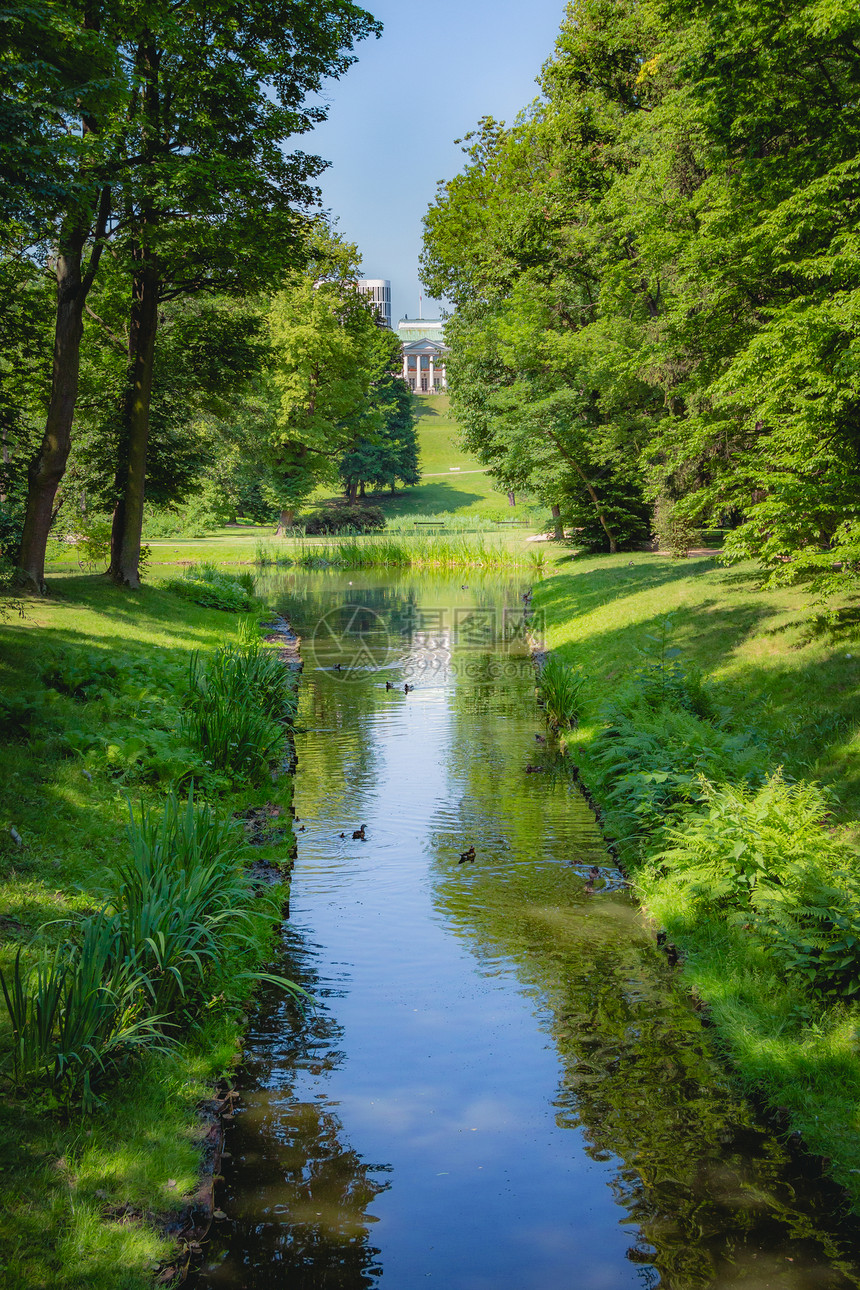 在华沙波兰Lazienki公园的地平线上有绿草和树的美丽溪流以及Belweder宫图片