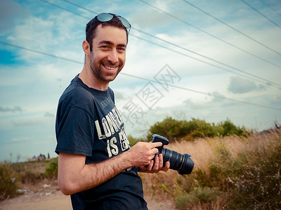 带着数码相机的摄影师手持数码相机向野外的摄影机微笑图片