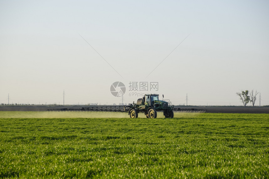 高轮式拖拉机正在对青小麦施肥使用细散喷雾化学品日落背景的拖拉机高轮式正在对青小麦施肥图片