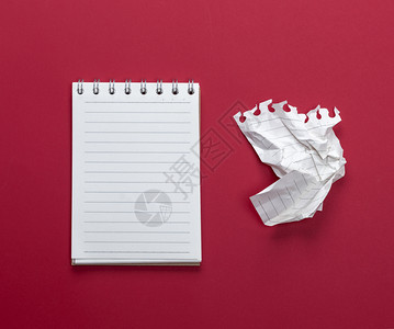 张开笔记本上面有白的床单和一块碎纸在红色背景的纸上撕扯出来背景图片