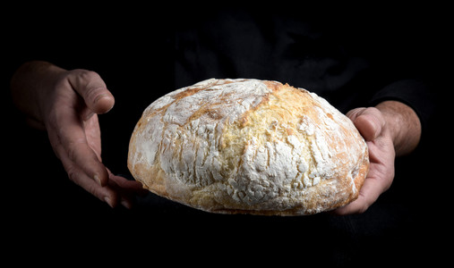 男厨师手握着一整卷面包圆黑色背景图片