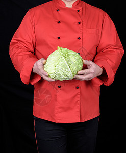 穿红制服的厨师拿着一整包卷心菜黑色背景图片