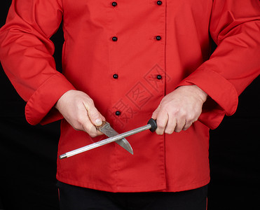 穿红制服的厨师磨利一把刀黑色背景的图片