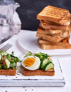 白面上包的正方白木板早餐三明治上加煮鸡蛋黄瓜和绿菠菜叶图片