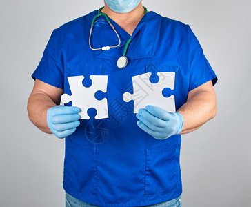 蓝色制服和无菌乳胶手套的医生持有白色大空拼图灰色背景图片