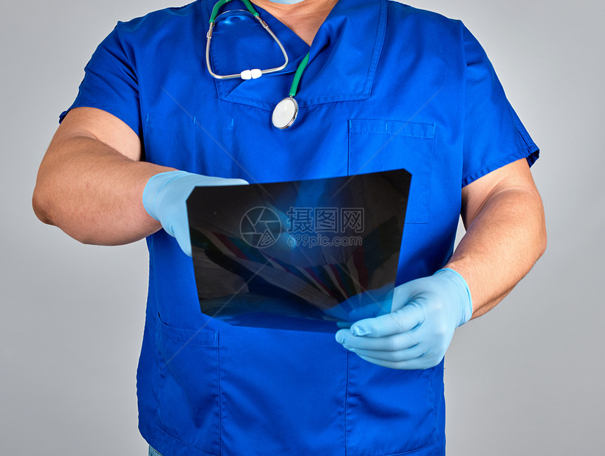 蓝制服医生和无菌乳胶手套持有和检查灰底腿骨X光图片