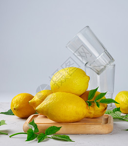 新鲜成熟的全黄柠檬和木板上两杯子用于制作夏季饮料的原图片