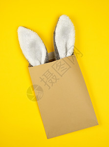 棕色手工艺信封黄色背景装有兔子耳朵图片