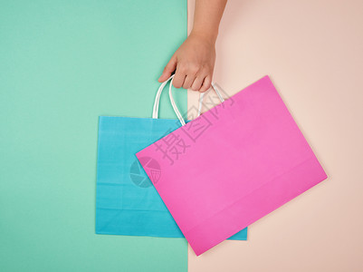 手握两个彩色背景的纸质购物袋具有季节销售的概念图片
