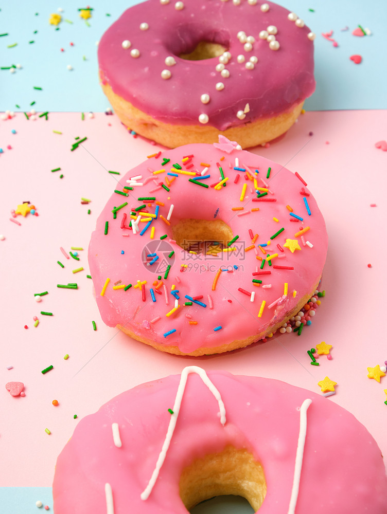 三个不同的甜圈喷洒在粉红色背景上最观关闭图片