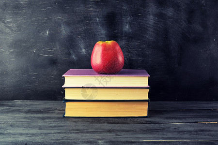 红苹果躺在一堆书上黑色背景回到学校图片