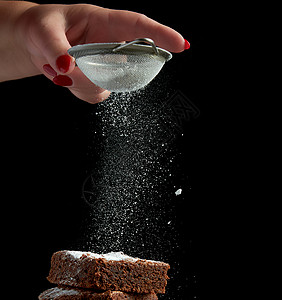 方形的烤巧克力蛋糕片上撒着白糖从铁筛上小颗粒飞下来低调图片