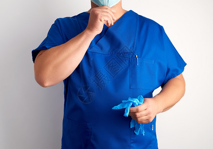 穿蓝制服的医生持有不消毒的乳胶手套并戴上白底面具图片