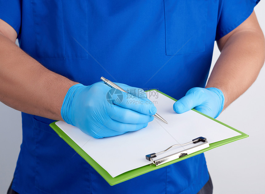 穿蓝色制服和乳胶手套的医生持有一张绿色纸页用右手写作贴上图片