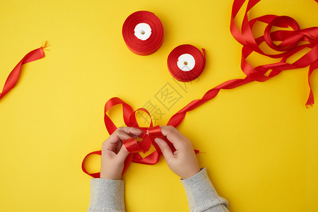 姜黄色丝带两只母的手绑着弓和红丝带两只领在黄底的顶视面背景