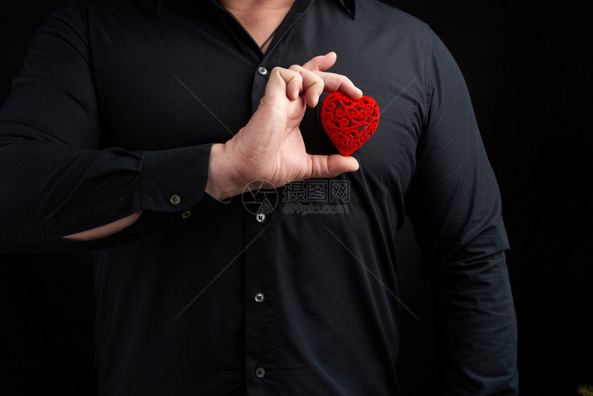 成人男子身穿黑衬衫背着暗景身衬衫在右手胸前握着红心将爱的概念放在胸前图片