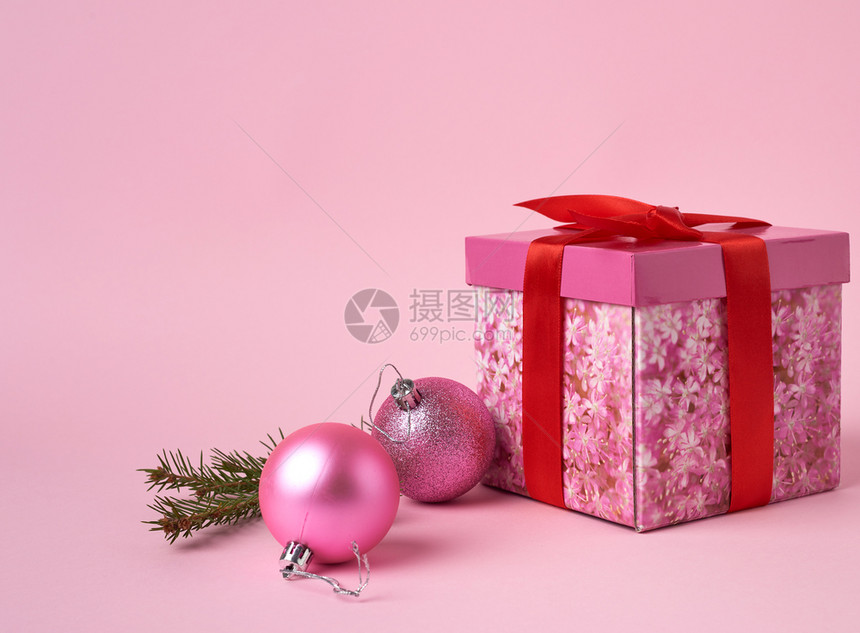 粉红色礼物盒有弓绿色树枝和粉红背景上两个装饰粉红色球图片