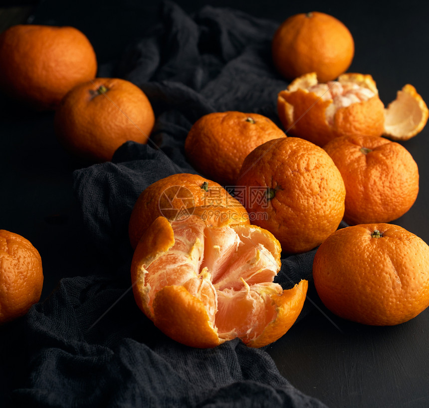 磨熟的橙色曼达林和一堆未熟的圆全果子在黑餐巾纸上低键图片