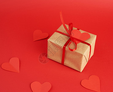 用棕色工艺纸包着礼物的方形盒子在红色的背景上系上一条薄薄的丝绸红丝带空纸心形的礼物背景图片