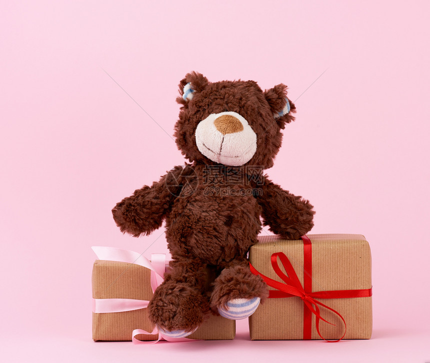 棕褐色可爱的泰迪熊和包在棕色生态纸上绑在粉红背景情人节生日庆背景的彩带上礼物图片