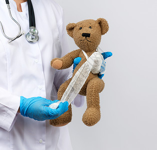 女医务员持有棕色泰迪熊和白纱布绷带儿科和动物治疗概念的绷带爪背景图片