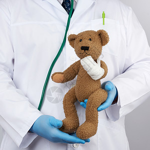 穿白外套的儿科医生蓝色的乳胶手套带着棕色泰迪熊图片