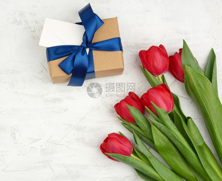 红色盛开的郁金香花束上面有绿色叶子白背景的棕手纸包着礼物复制空间生日情人节的喜悦背景图片