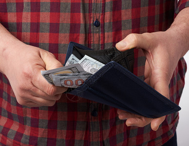 身穿格斗红衬衫的男人拿着一个钱包满百美元纸币钞票工资概念财富方格高清图片素材