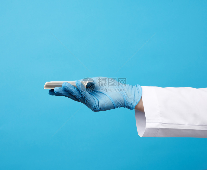 医生用蓝色胶手套在蓝色背景登记地点的空白纸面名片上持有一张空白纸面名片图片