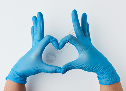 丁腈手套用蓝色的乳胶不育医疗手套用两只握着蓝乳胶不育的手套展示了白种背景善良概念帮助和志愿工作的心脏姿态背景