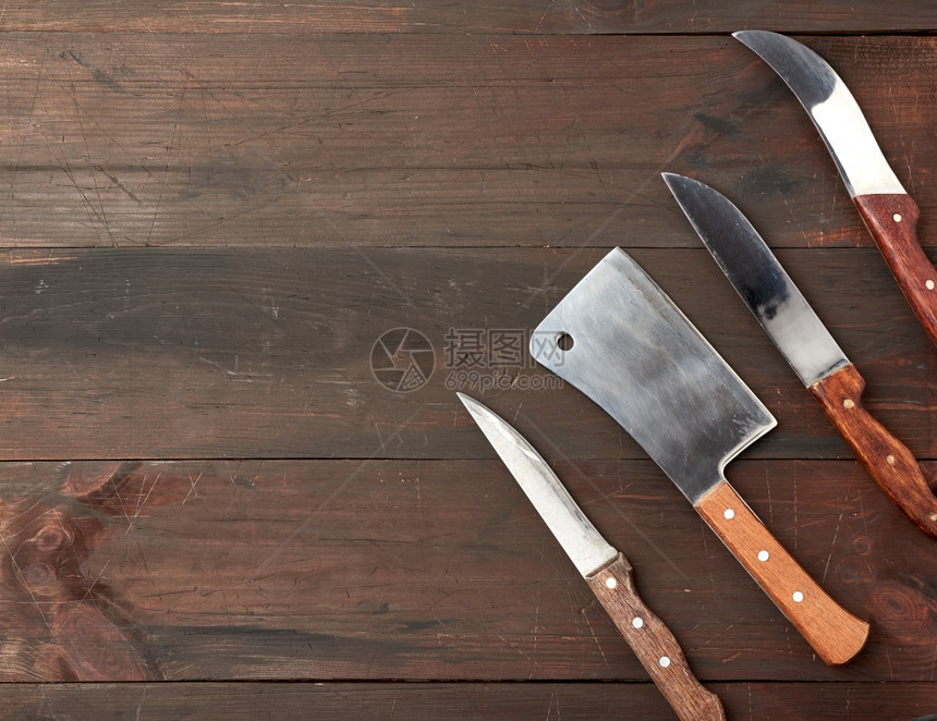 由不同的厨房刀组成用木柄从板顶视面的棕色背景图片