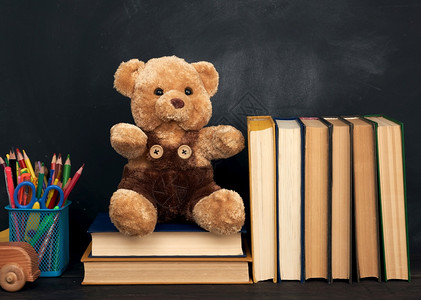 棕褐色泰迪熊坐在棕木桌上坐在空黑粉笔板后面回到学校背景图片