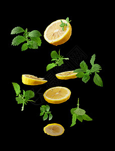 熟的多汁黄柠檬片和盛满薄荷的绿色叶子在黑背景的空气中漂浮饮料的成分图片