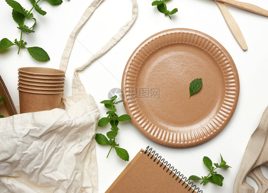 棕色手工艺纸白背景的绿薄荷叶棕手纸的纺织袋和一次餐具白色背景的绿薄荷叶图片