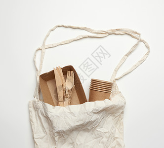 白色背景的棕手工艺纸上的白色纺织品袋和一次餐具图片