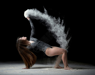 长发的年轻美女穿着运动服坐在地板上向她扔白面粉黑色背景背景图片