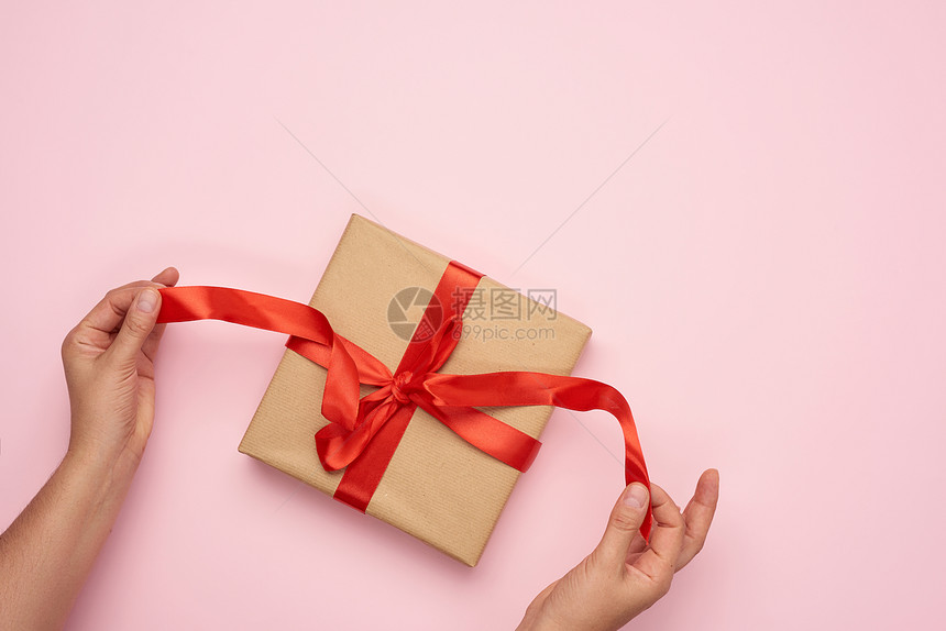 红丝带绑在包粉红背景的棕色Kraft纸上的礼物图片