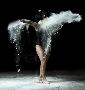 一位身材健壮的女子在黑色背景上的白色面粉中翩翩起舞舞者身穿黑色紧身衣图片