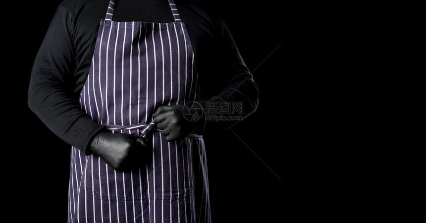 一个穿条纹蓝色围裙和黑衣服的男厨站在黑色背景上作一个刻字的地方图片