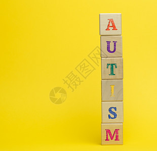 多彩立方体在黄色背景上刻有自闭症的木制板立方体支持和鼓励有大脑发育障碍的儿童概念复制空间背景